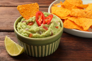 Photo of Bowl of delicious guacamole, nachos chips and lime on wooden table, closeup