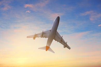 Airplane flying in cloudy sky at sunset. Air transportation