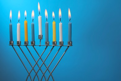Photo of Hanukkah celebration. Menorah with burning candles on light blue background, space for text