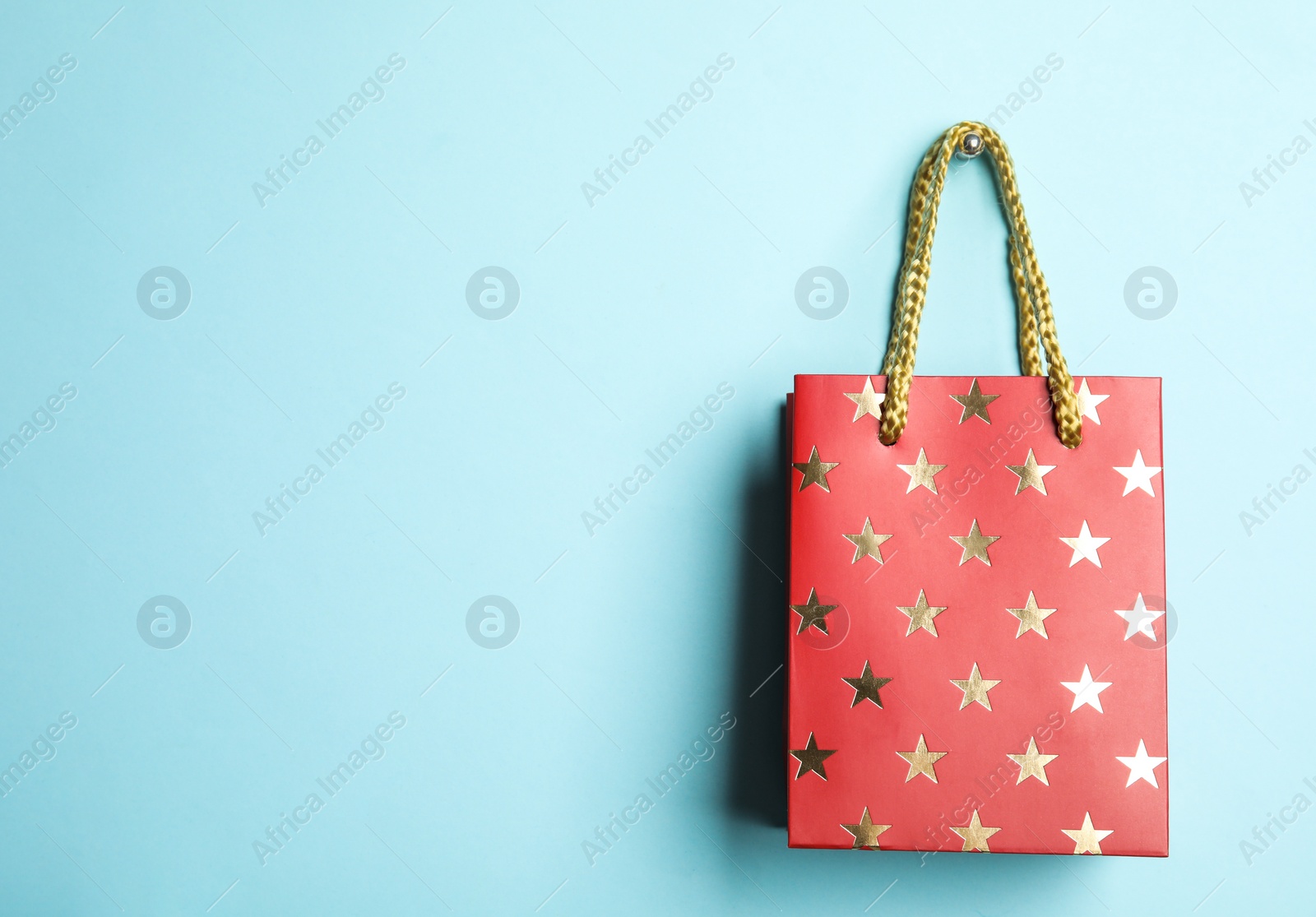 Photo of Red shopping paper bag with star pattern on light blue background, space for text