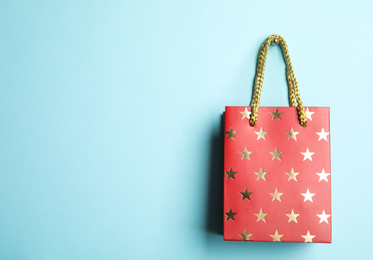 Red shopping paper bag with star pattern on light blue background, space for text