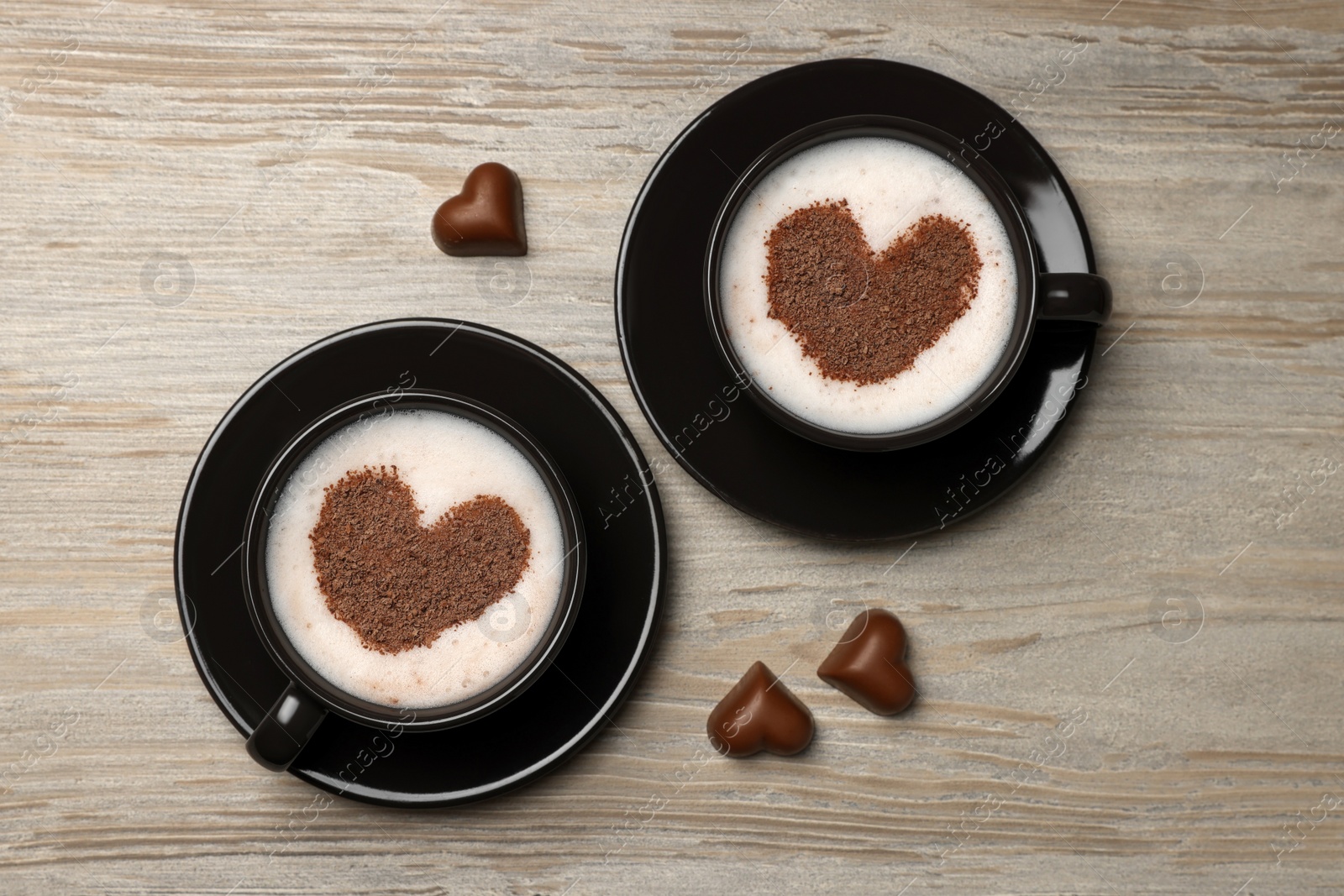 Photo of Cups of aromatic coffee with heart shaped decoration and chocolate candies on wooden table, flat lay