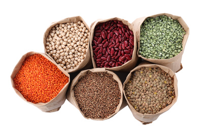 Different types of legumes and cereals in paper bags on white background, top view. Organic grains