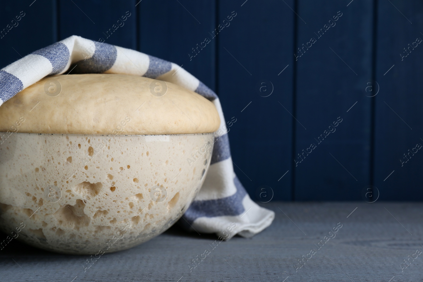 Photo of Bowl of fresh yeast dough on grey wooden table. Space for text