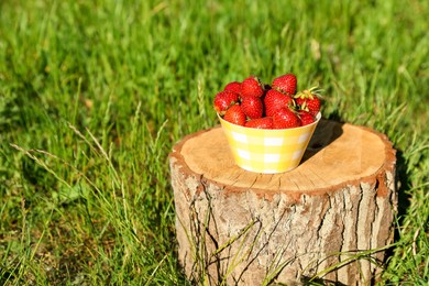 Photo of Bowl of ripe strawberries on tree stump outdoors. Space for text