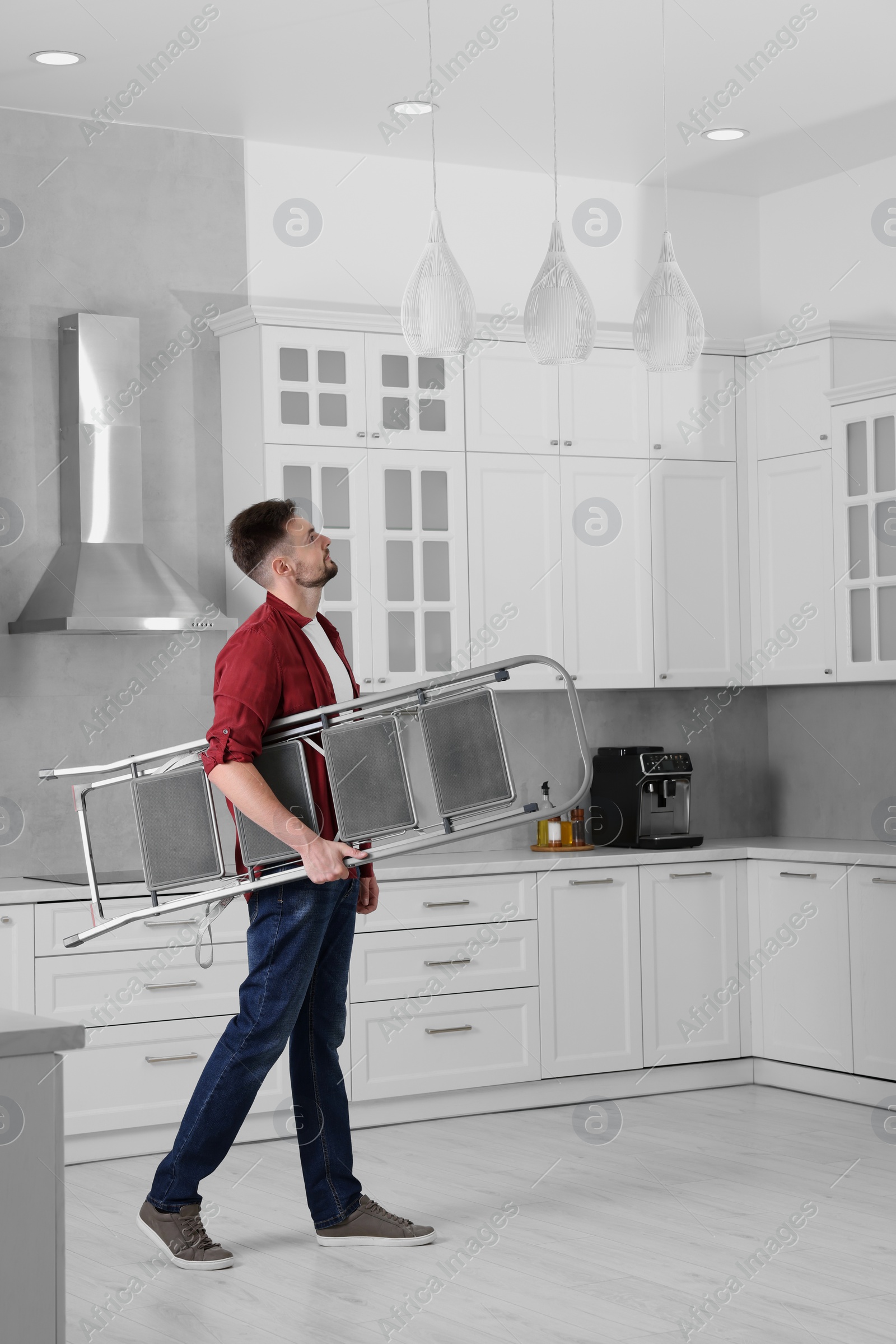 Photo of Young man carrying metal stepladder in kitchen