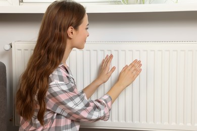 Photo of Woman warming hands on heating radiator near white wall