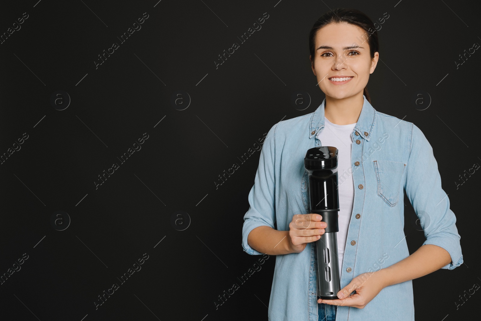 Photo of Beautiful young woman holding sous vide cooker on black background. Space for text