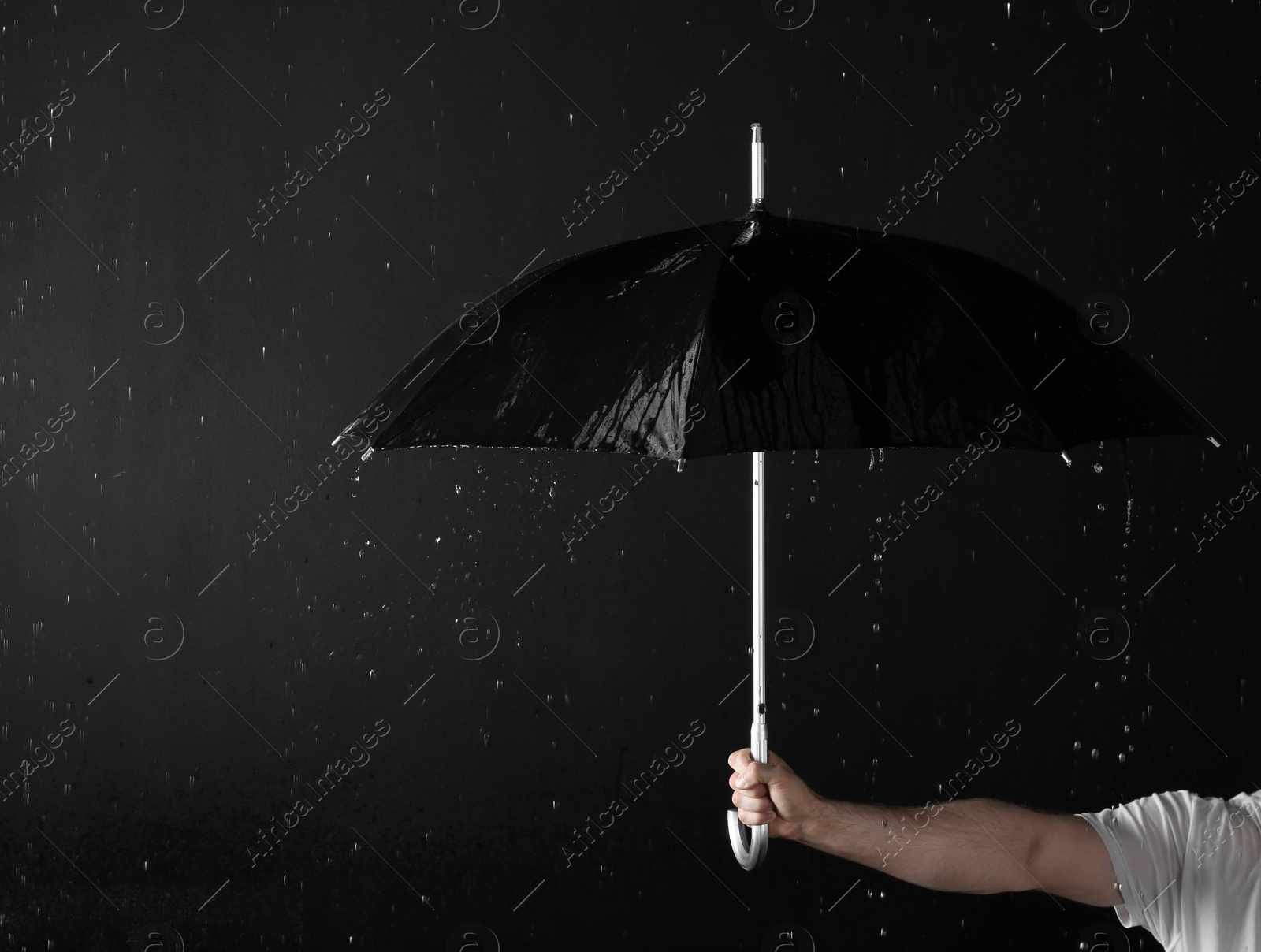 Photo of Man holding black umbrella under rain against dark background, closeup