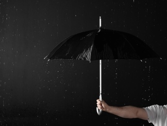 Photo of Man holding black umbrella under rain against dark background, closeup