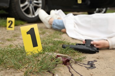 Crime scene markers, dead woman's body and gun outdoors, selective focus