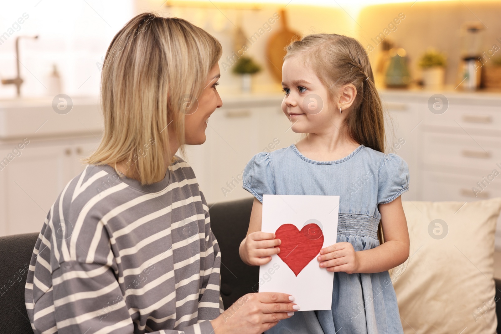 Photo of Little daughter congratulating her mom with greeting card at home. Happy Mother's Day