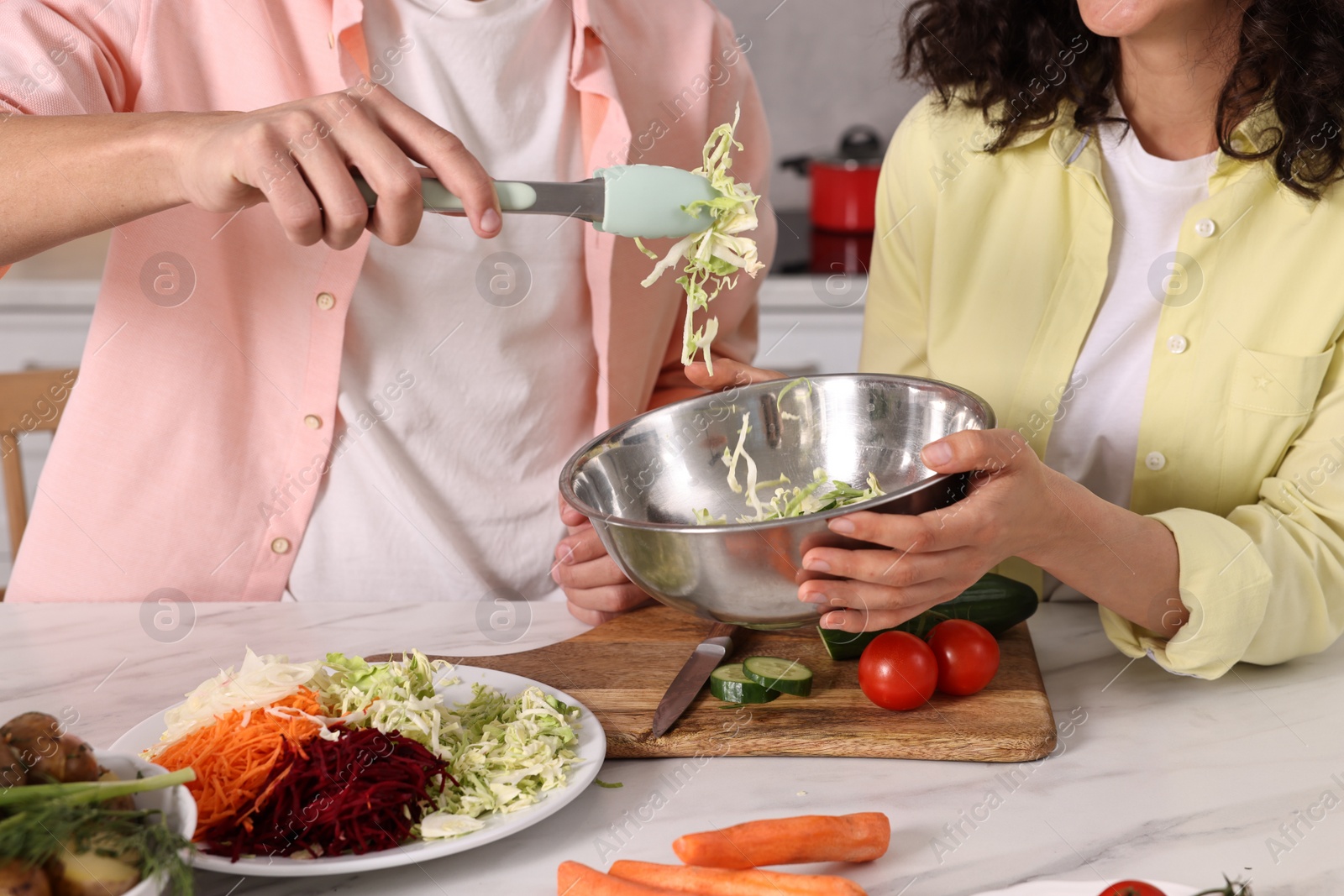 Photo of Friends cooking healthy vegetarian meal at white marble table in kitchen, closeup