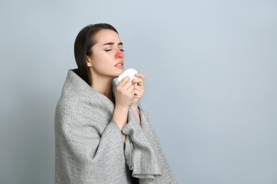 Young woman with blanket sneezing on light grey background, space for text. Runny nose