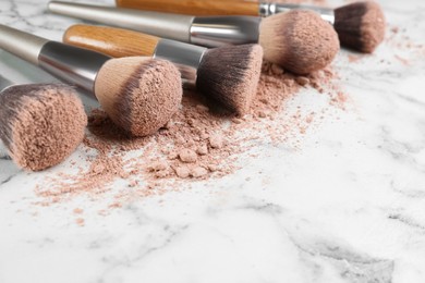 Photo of Different makeup brushes with crushed cosmetic product on white marble table, closeup. Space for text