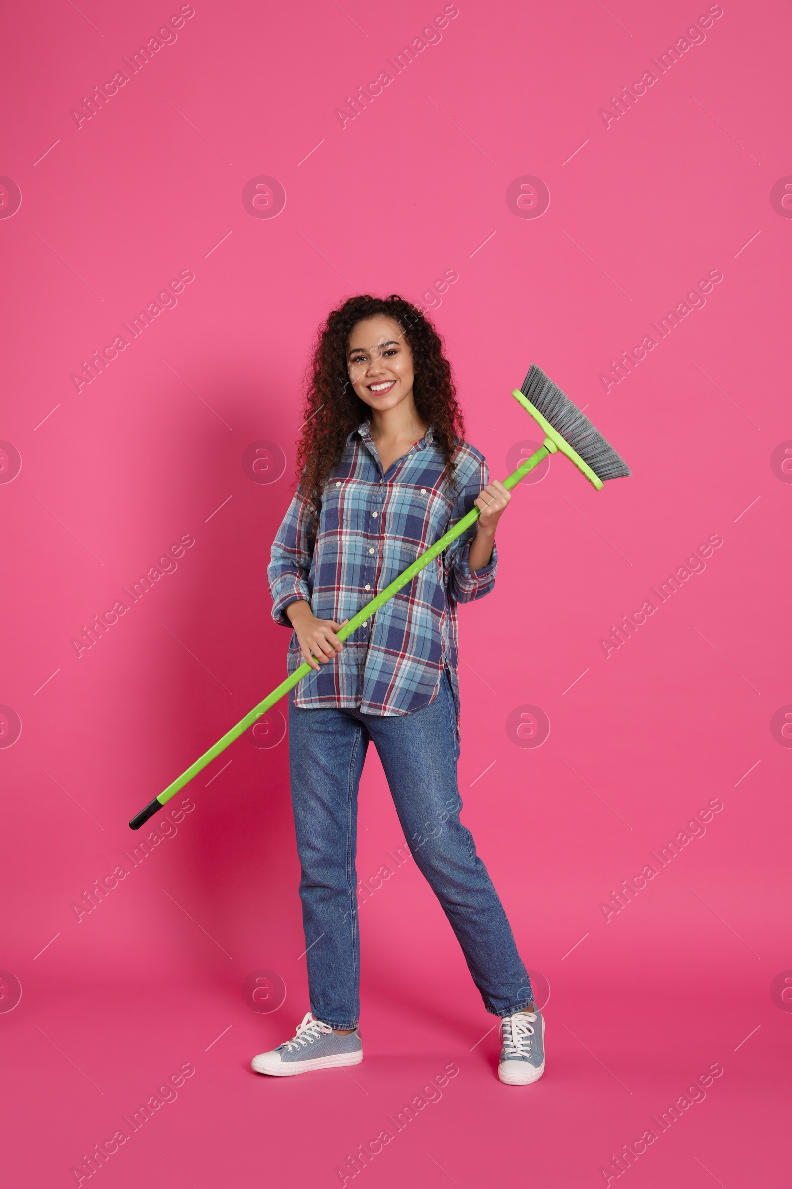 Photo of African American woman with green broom on pink background
