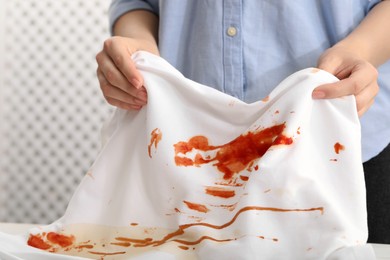 Photo of Woman holding shirt with stain of sauce on blurred background, closeup