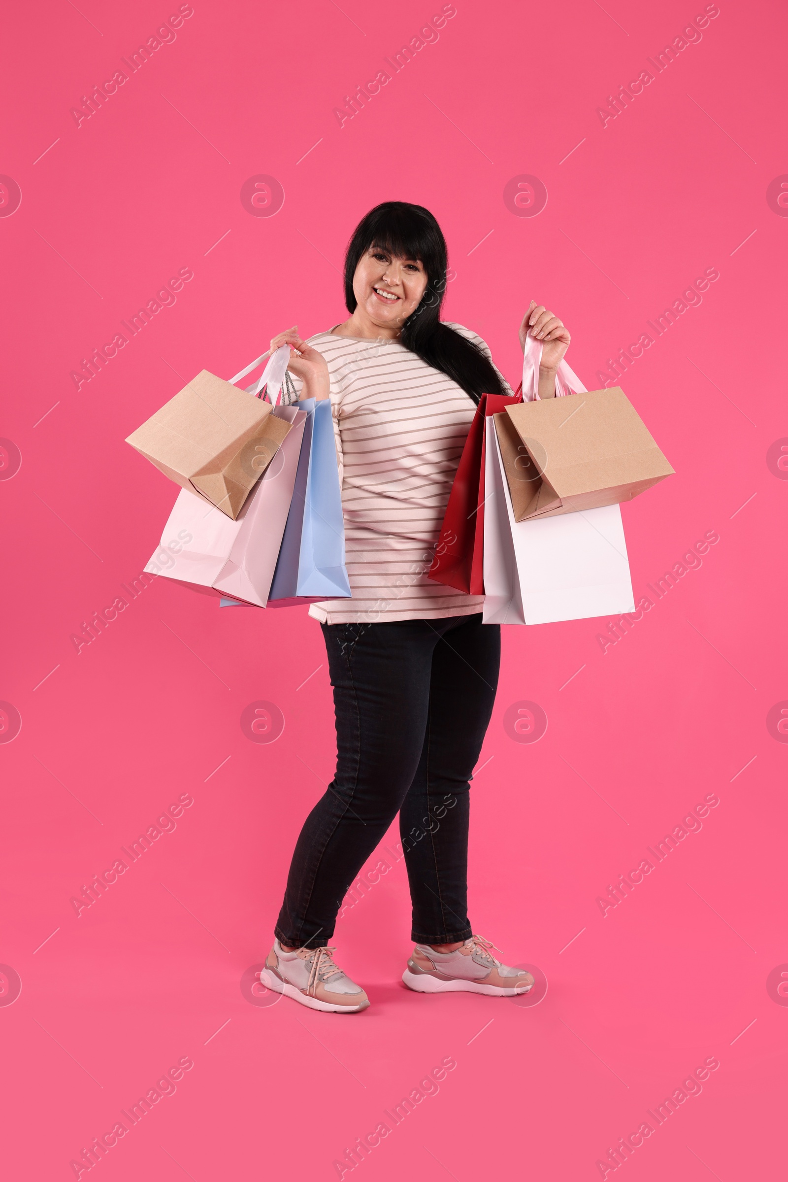 Photo of Beautiful overweight mature woman with shopping bags on pink background