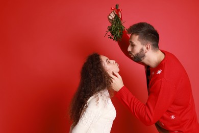 Photo of Lovely couple under mistletoe bunch on red background. Space for text