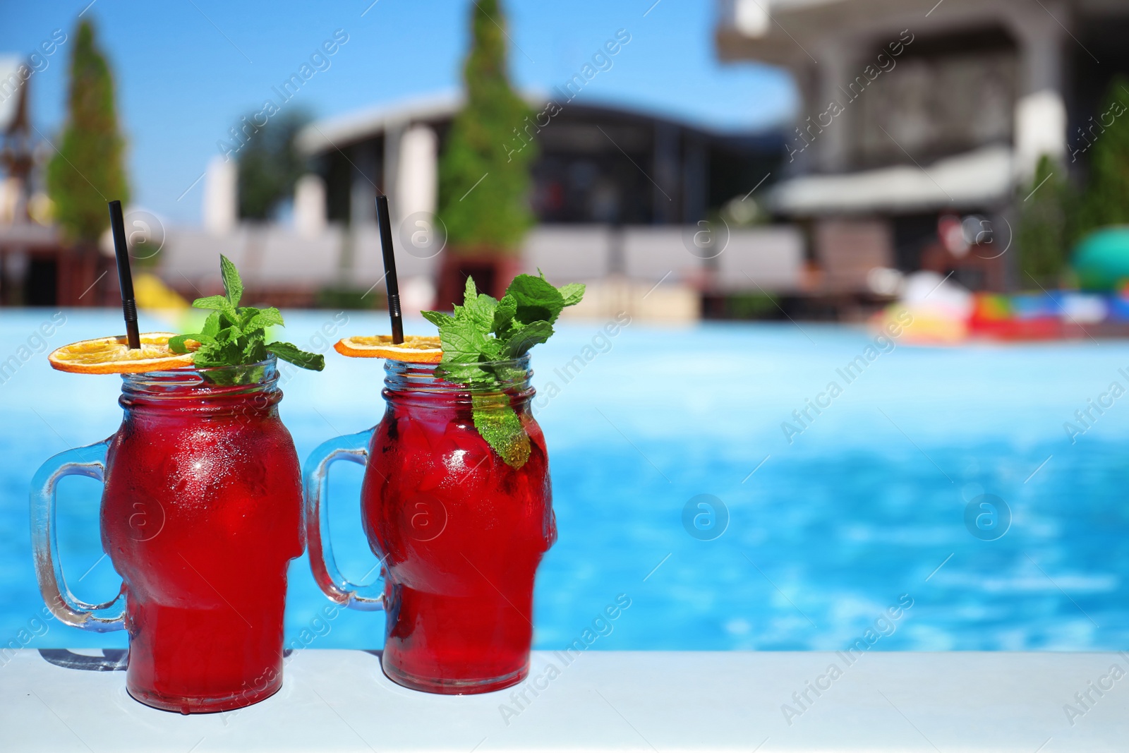 Photo of Mason jars with refreshing cocktail near swimming pool on sunny day. Space for text