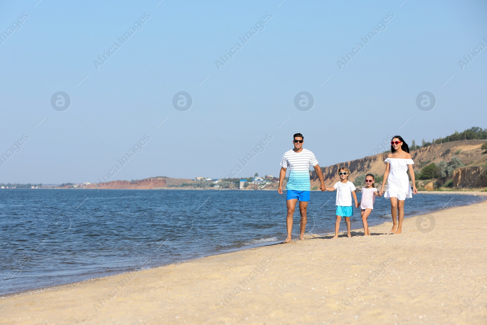 Photo of Happy family walking on sandy beach near sea, space for text. Summer holidays