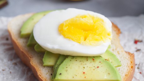 Photo of Delicious sandwich with boiled egg and pieces of avocado on table, closeup