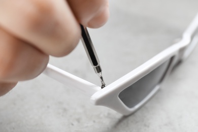 Handyman repairing sunglasses with screwdriver at grey table, closeup