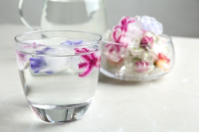 Glass of water with floral ice cubes on table. Space for text