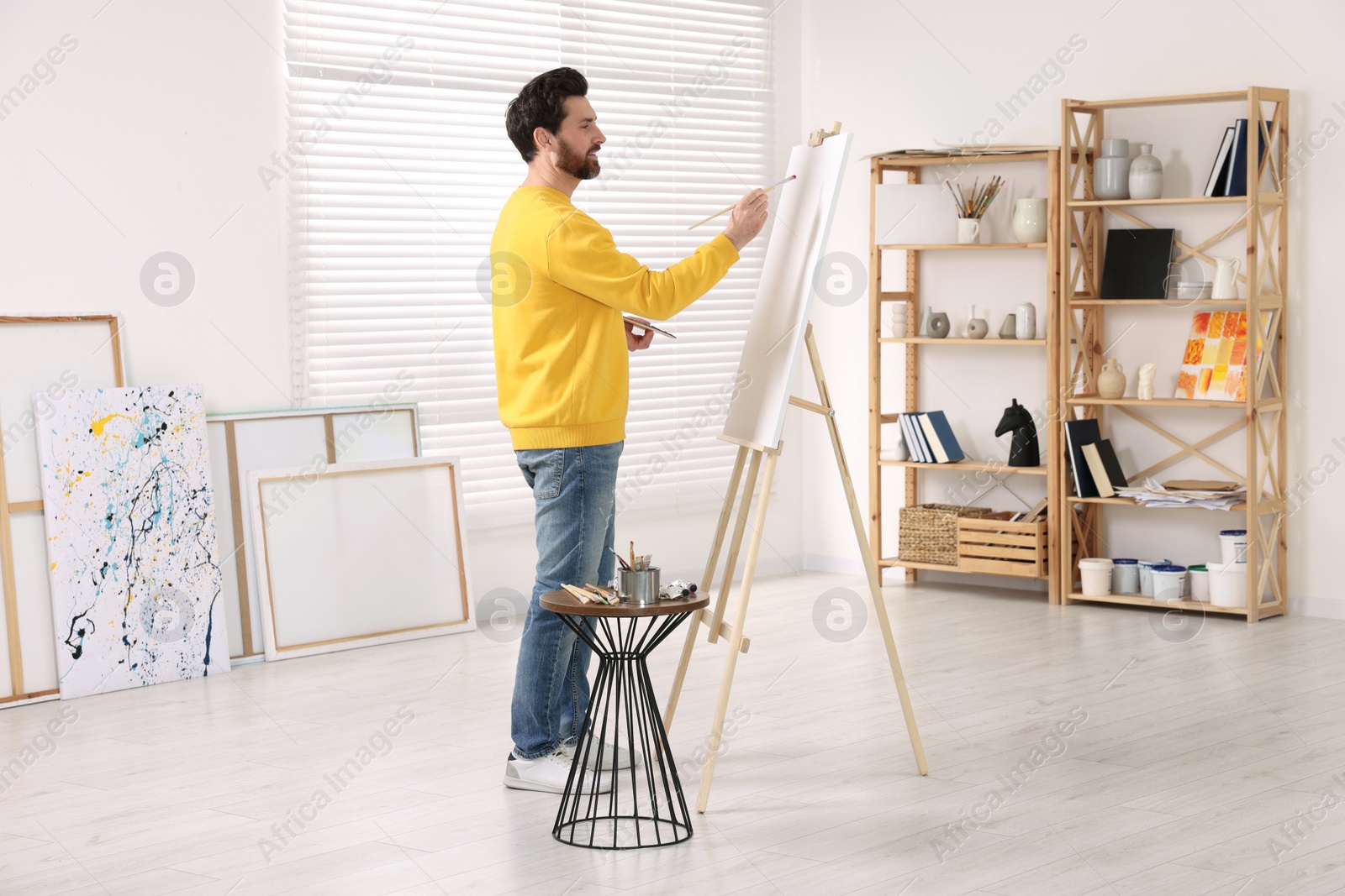 Photo of Man painting in studio. Using easel to hold canvas