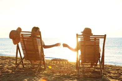 Couple relaxing on deck chairs at sandy beach. Summer vacation