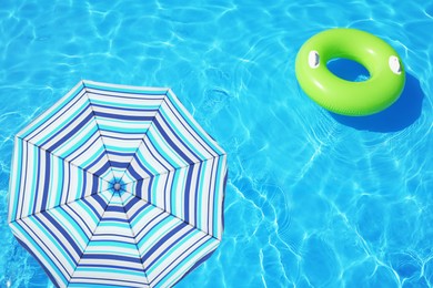 Image of Open beach umbrella and inflatable ring floating in swimming pool 