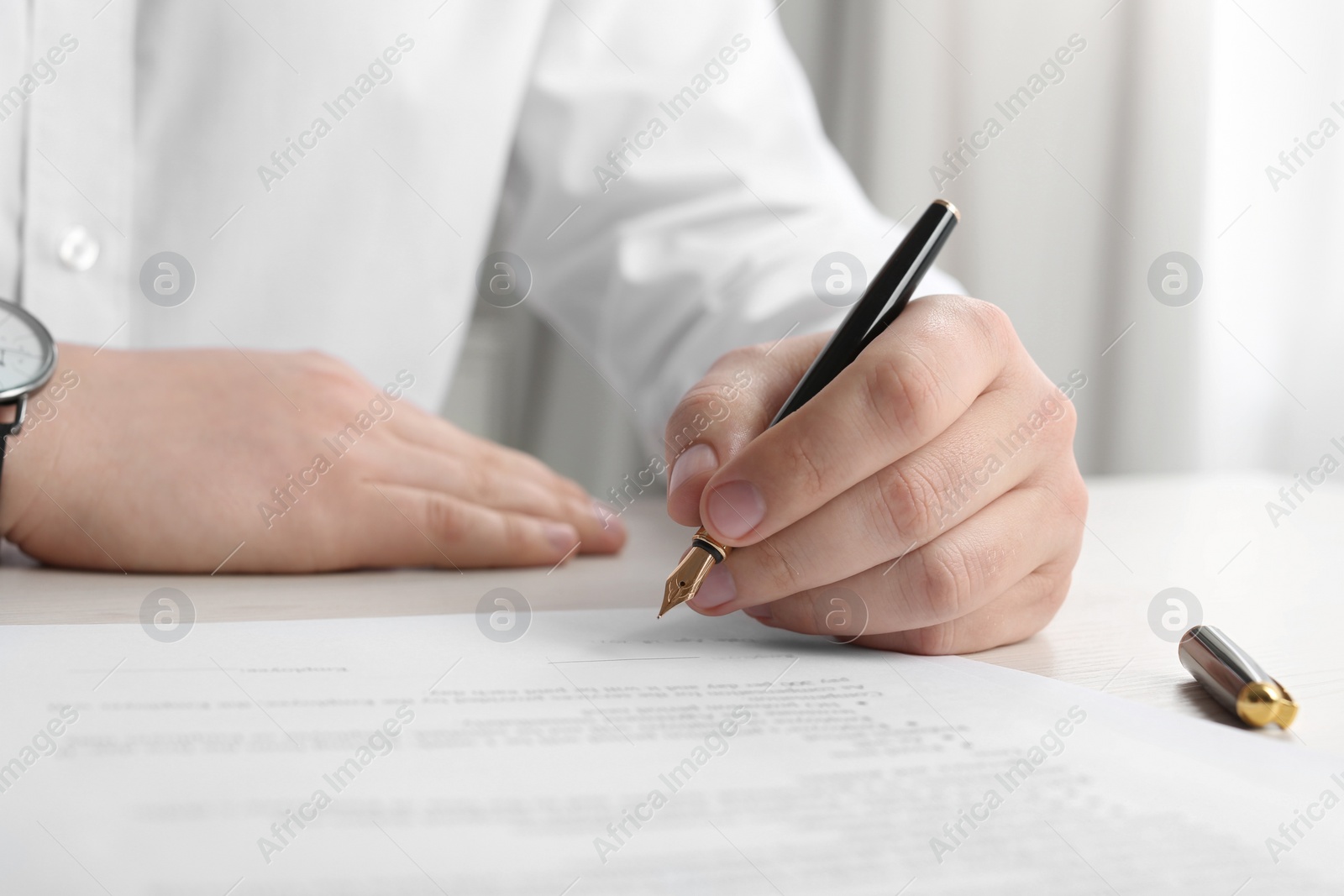 Photo of Notary signing document at wooden table indoors, closeup