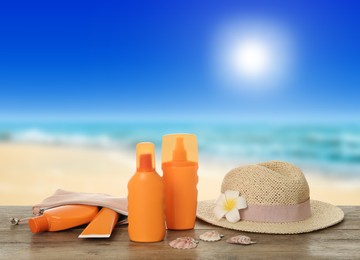 Image of Different skin sun protection products and hat on wooden table against seascape. Space for design