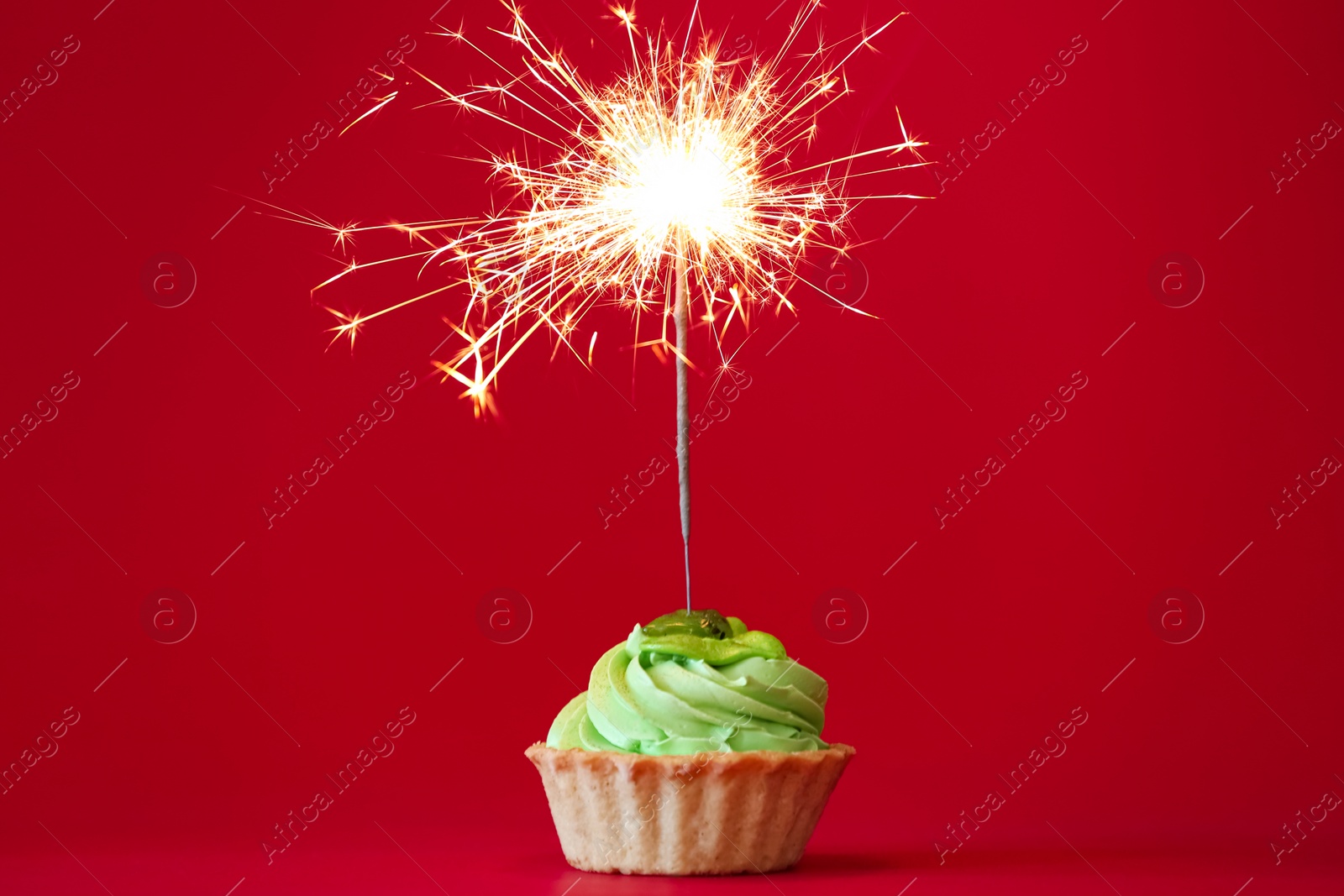 Photo of Cupcake with burning sparkler on red background