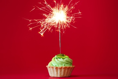 Photo of Cupcake with burning sparkler on red background