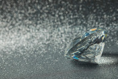 Photo of Beautiful dazzling diamond on shiny glitter background, space for text. Precious gemstone