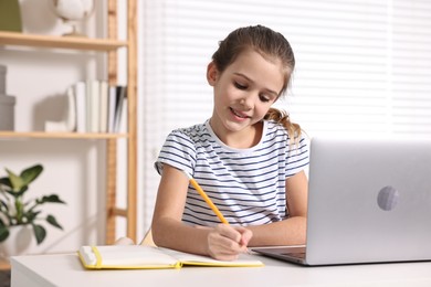 Photo of E-learning. Cute girl taking notes during online lesson at table indoors