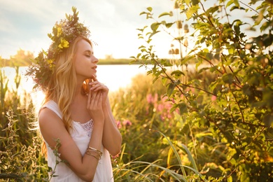 Photo of Young woman wearing wreath made of beautiful flowers outdoors on sunny day