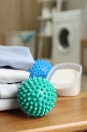 Photo of Dryer balls near stacked clean clothes and detergent on wooden table in laundry room
