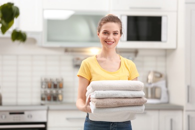 Woman holding folded clean towels in kitchen. Laundry day