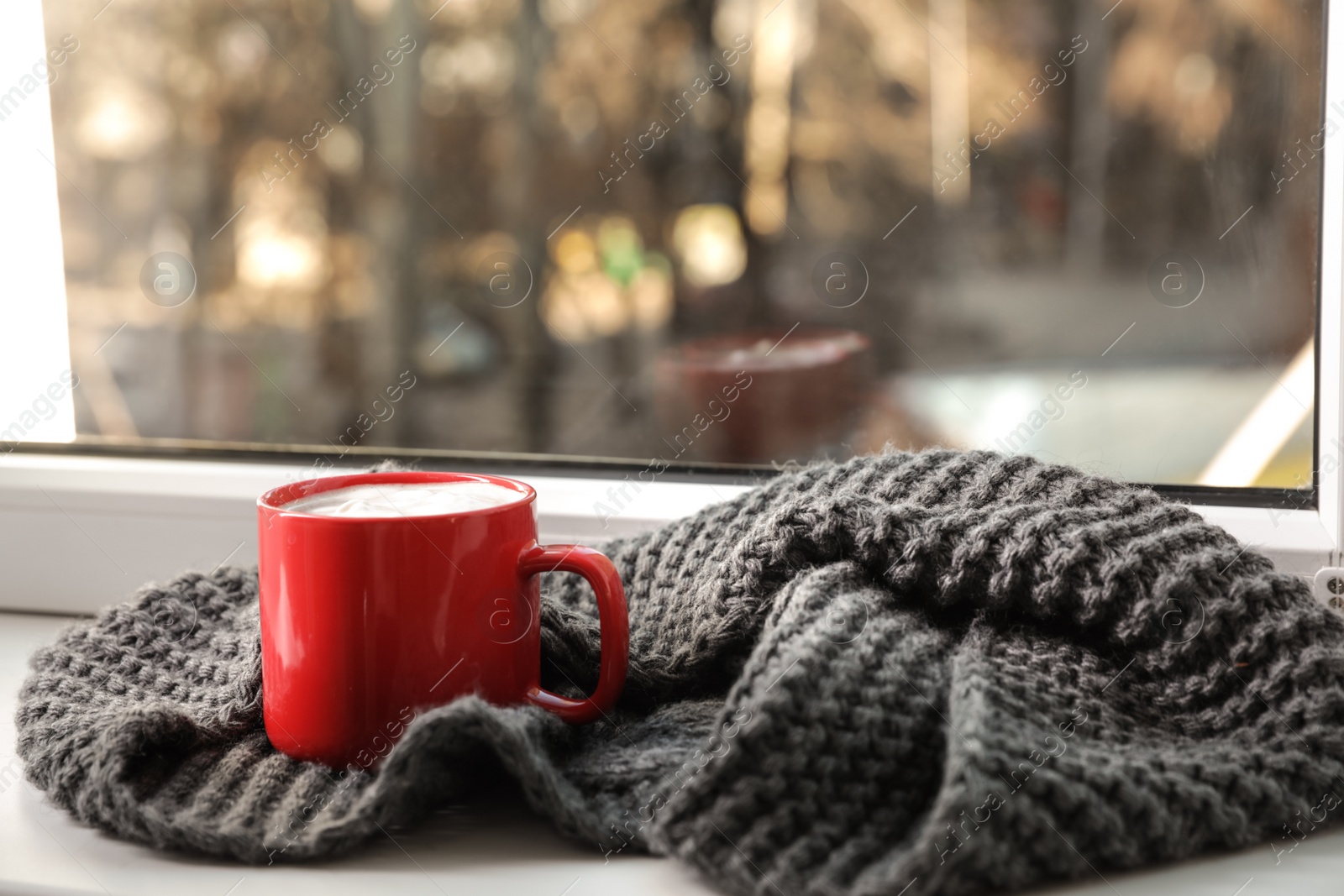 Photo of Cup of winter drink and knitted scarf on windowsill. Space for text