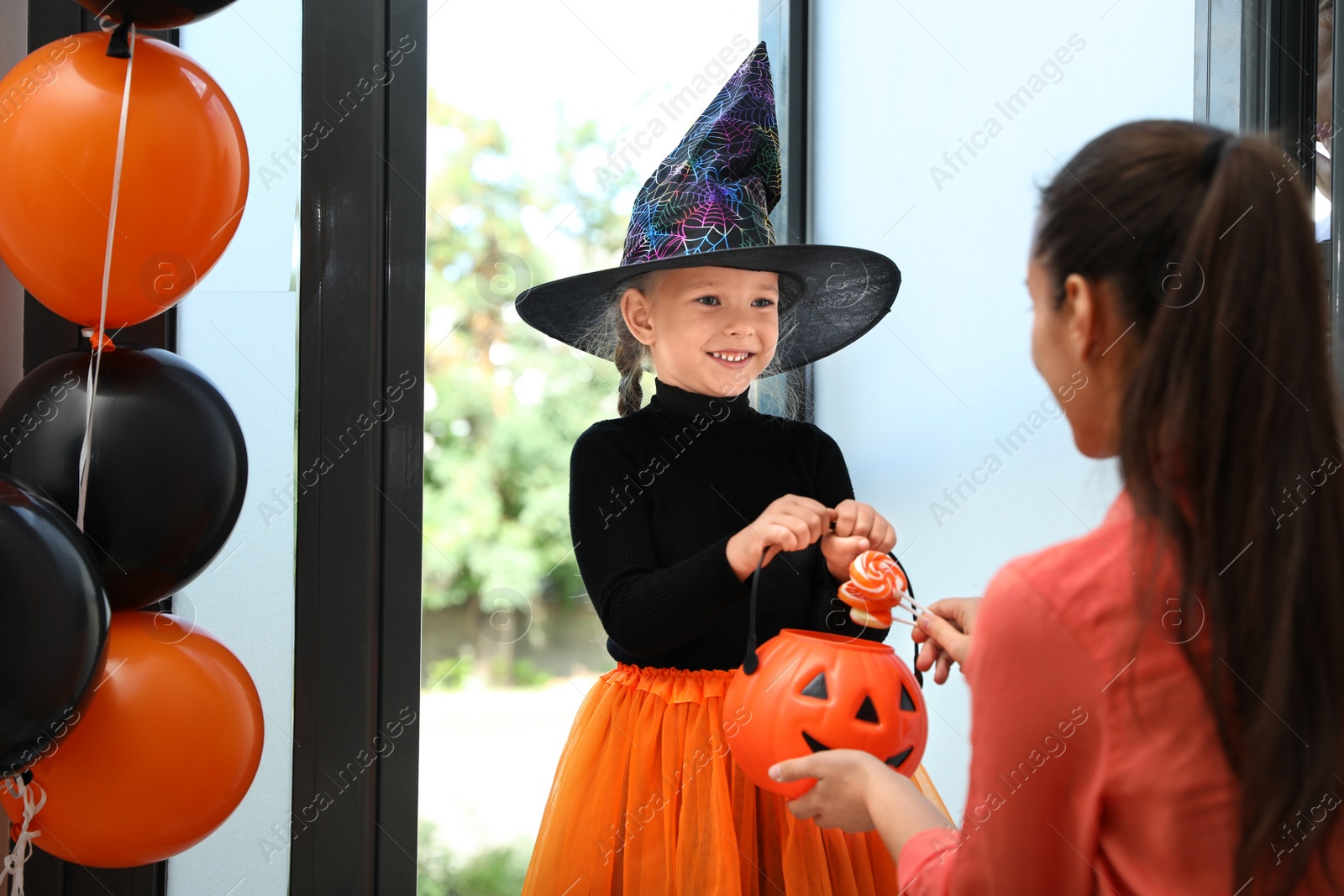 Photo of Cute little girl dressed as witch trick-or-treating at doorway. Halloween tradition