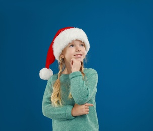 Photo of Cute little child wearing Santa hat on blue background. Christmas holiday