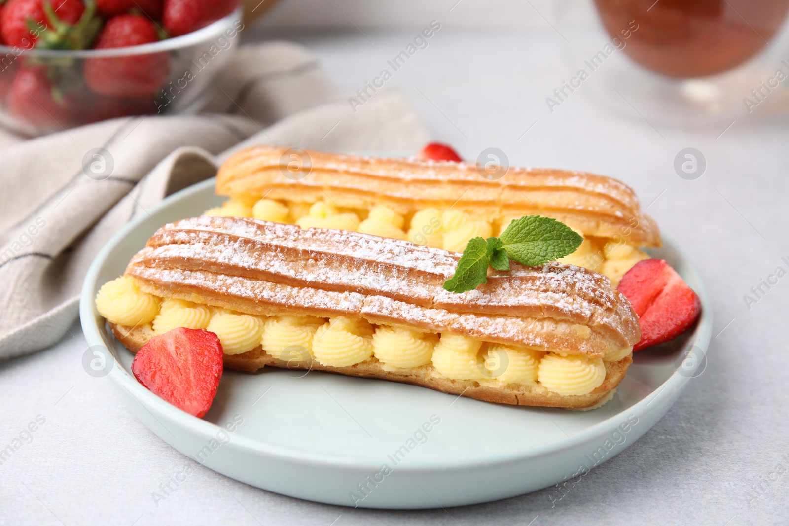 Photo of Delicious eclairs filled with cream, strawberries and mint on light table