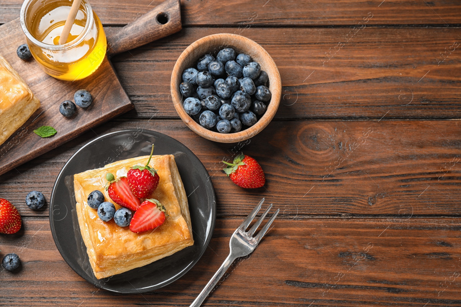 Photo of Fresh delicious puff pastry with sweet berries on wooden table, flat lay. Space for text