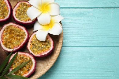 Halves of passion fruits (maracuyas), palm leaf and flowers on light blue wooden table, top view. Space for text