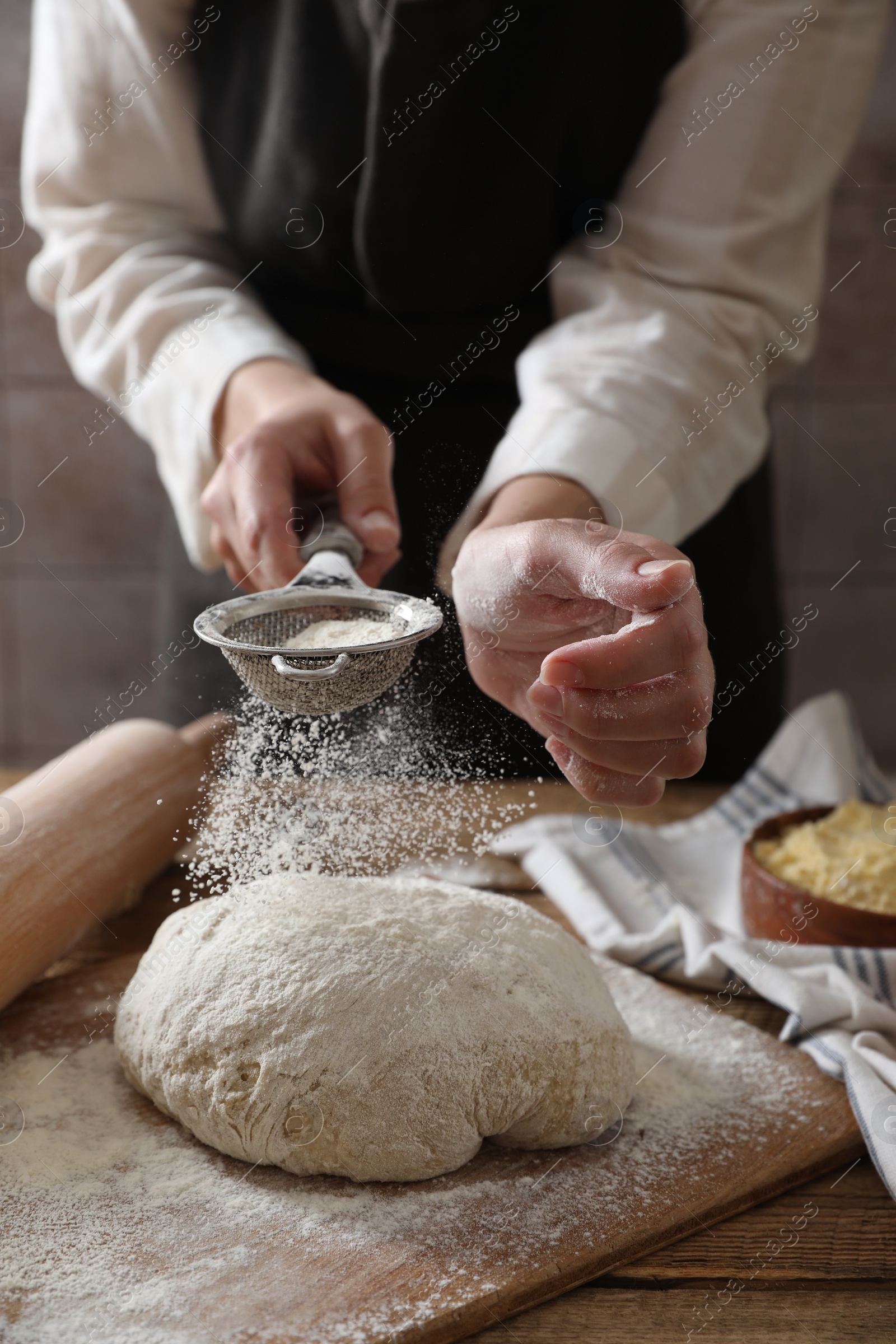 Photo of Woman sprinkling flour over dough at wooden table, closeup