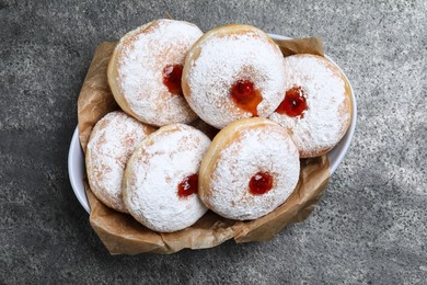Delicious donuts with jelly and powdered sugar in bowl on grey table, top view