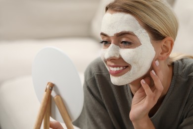Photo of Young woman with face mask looking into mirror on sofa. Spa treatments