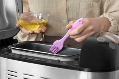 Photo of Woman spreading breadmaker pan with oil, closeup